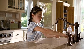 Ung jente vasker hendene i kjøkkenvask
