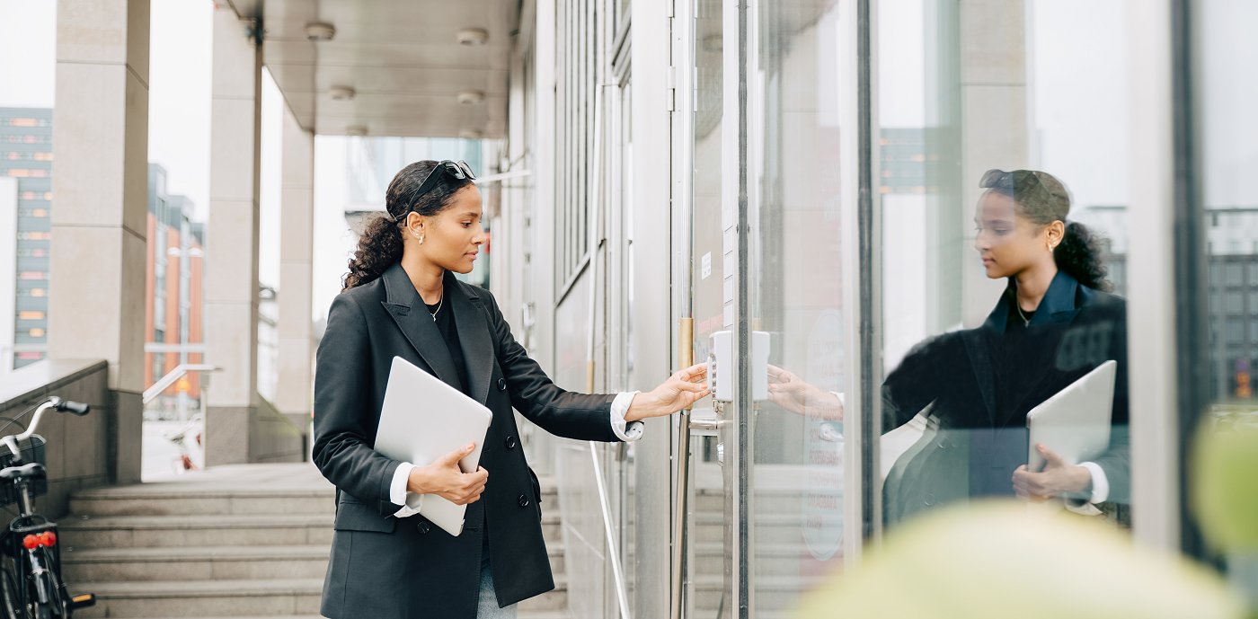 Kvinne taster inn kode på inngangsdør til kontorbygg Kvinne taster inn kode på inngangsdør til kontorbygg