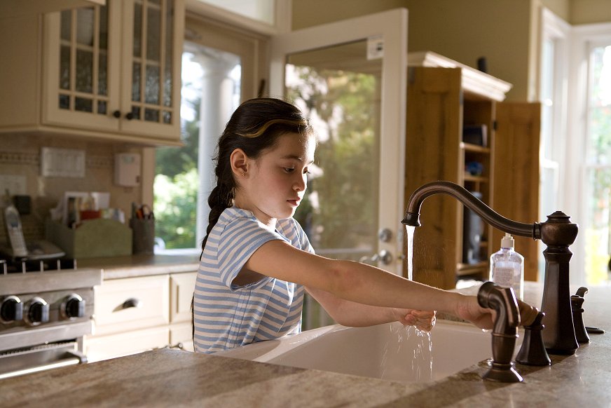 Ung jente vasker hendene i kjøkkenvask