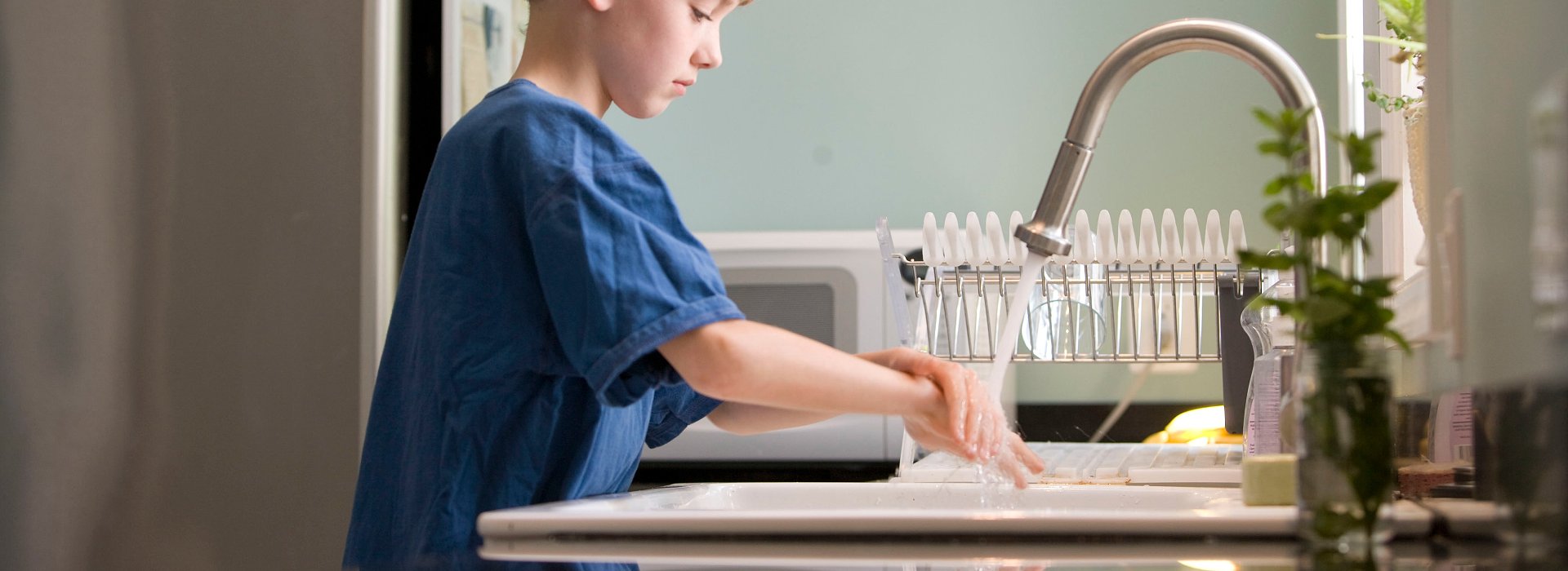 Ung gutt vasker hendene i kjøkkenvask
