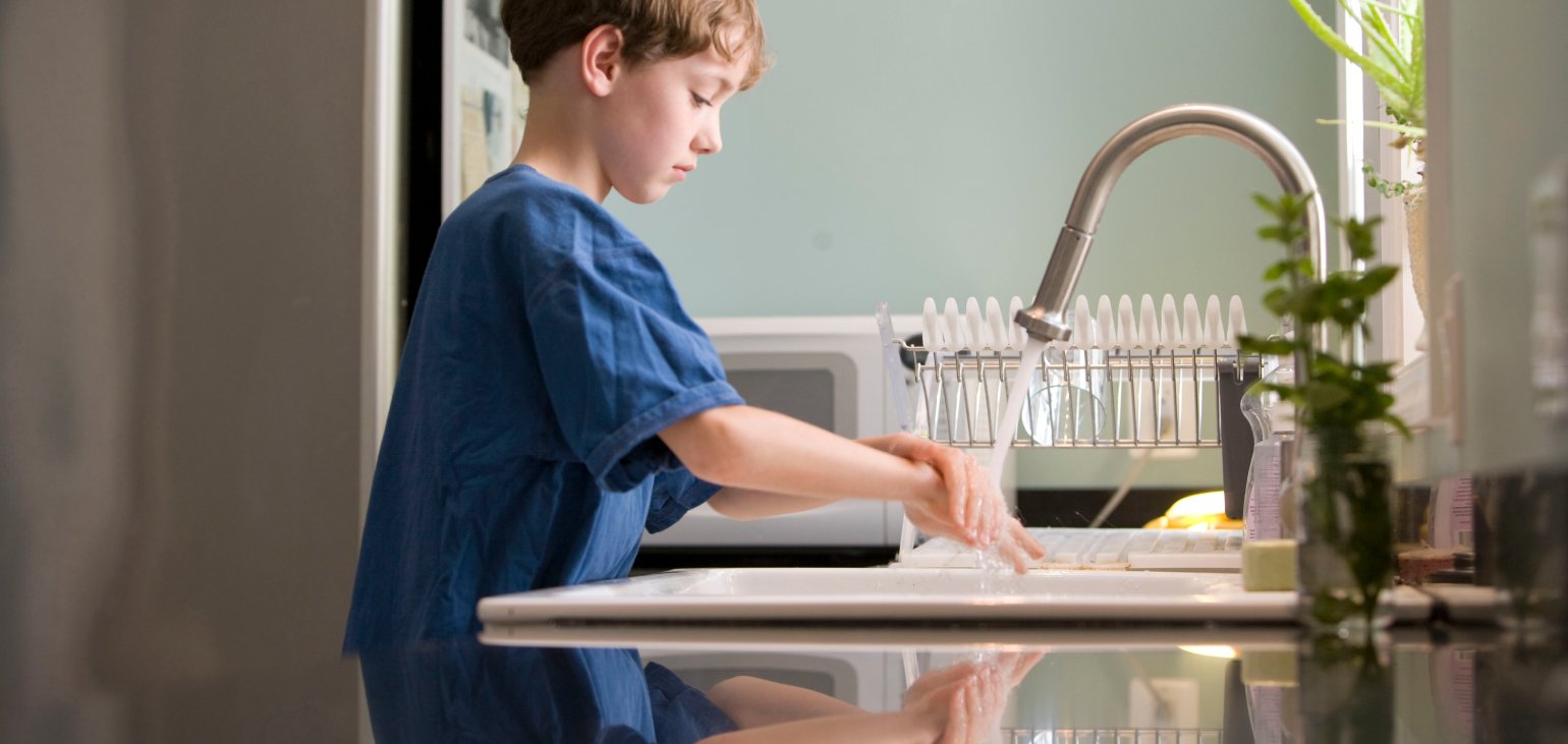 Ung gutt vasker hendene i kjøkkenvask