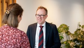 Bilde av konsernsjef i GK, Kim Robert Lisø, i samtale med ansatt i GK, tatt innendørs med planter i bakgrunnen.