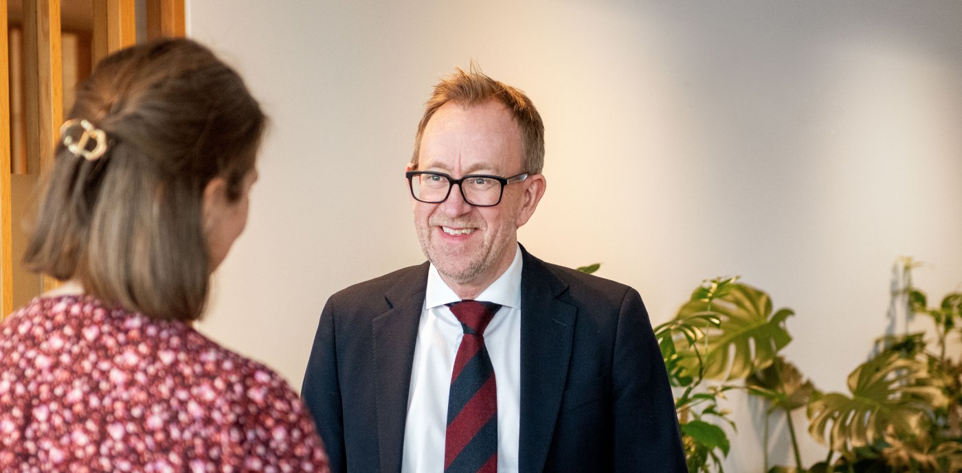 Bilde av konsernsjef i GK, Kim Robert Lisø, i samtale med ansatt i GK, tatt innendørs med planter i bakgrunnen.