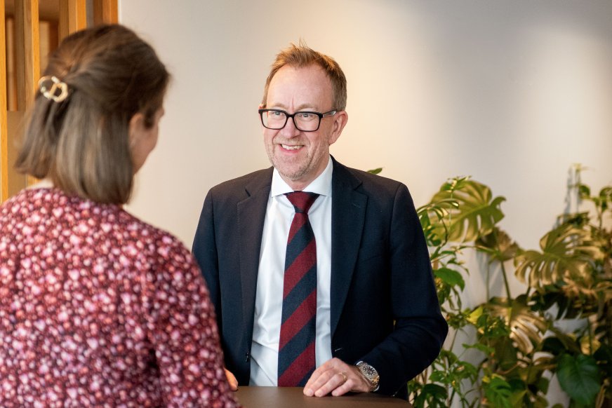 Bilde av konsernsjef i GK, Kim Robert Lisø, i samtale med ansatt i GK, tatt innendørs med planter i bakgrunnen.