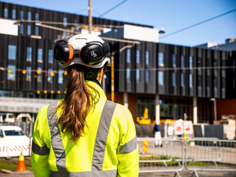 Brita Sandland i GK stående foran Livsvitenskapsbygget i Oslo med fullt værneutstyr, med ryggen til kamera.